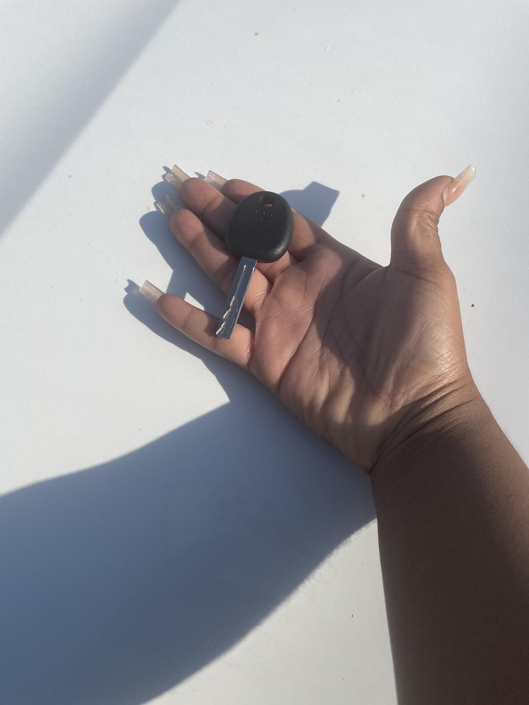 A freshly cut transponder car key resting in a customer's open hand, in bright sunlight